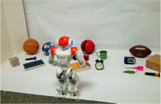 A robot standing in front of a white surface containing a variety of household objects.